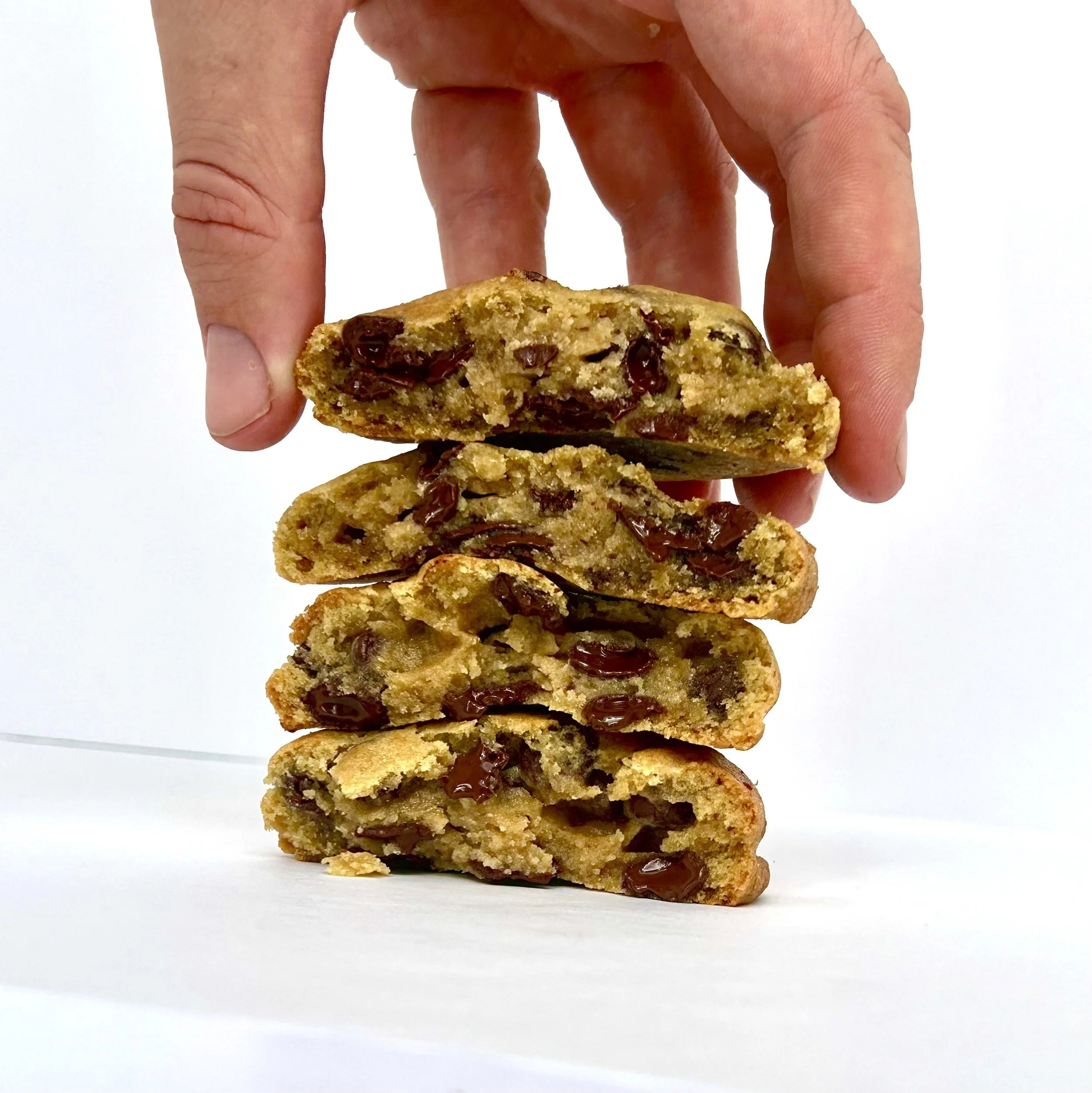 A hand stacking five chocolate chip cookies with visible chocolate chunks, placed against a white background.