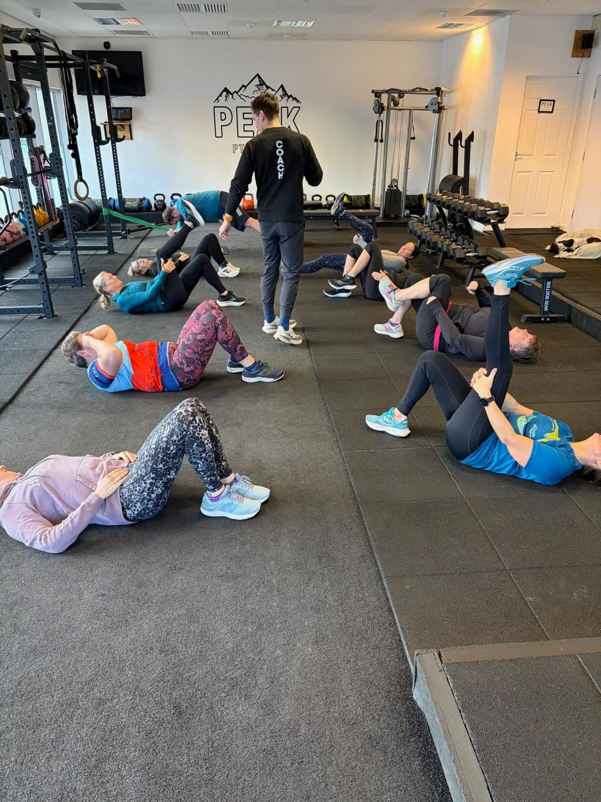 Group of women doing floor exercises in a gym with a coach supervising.