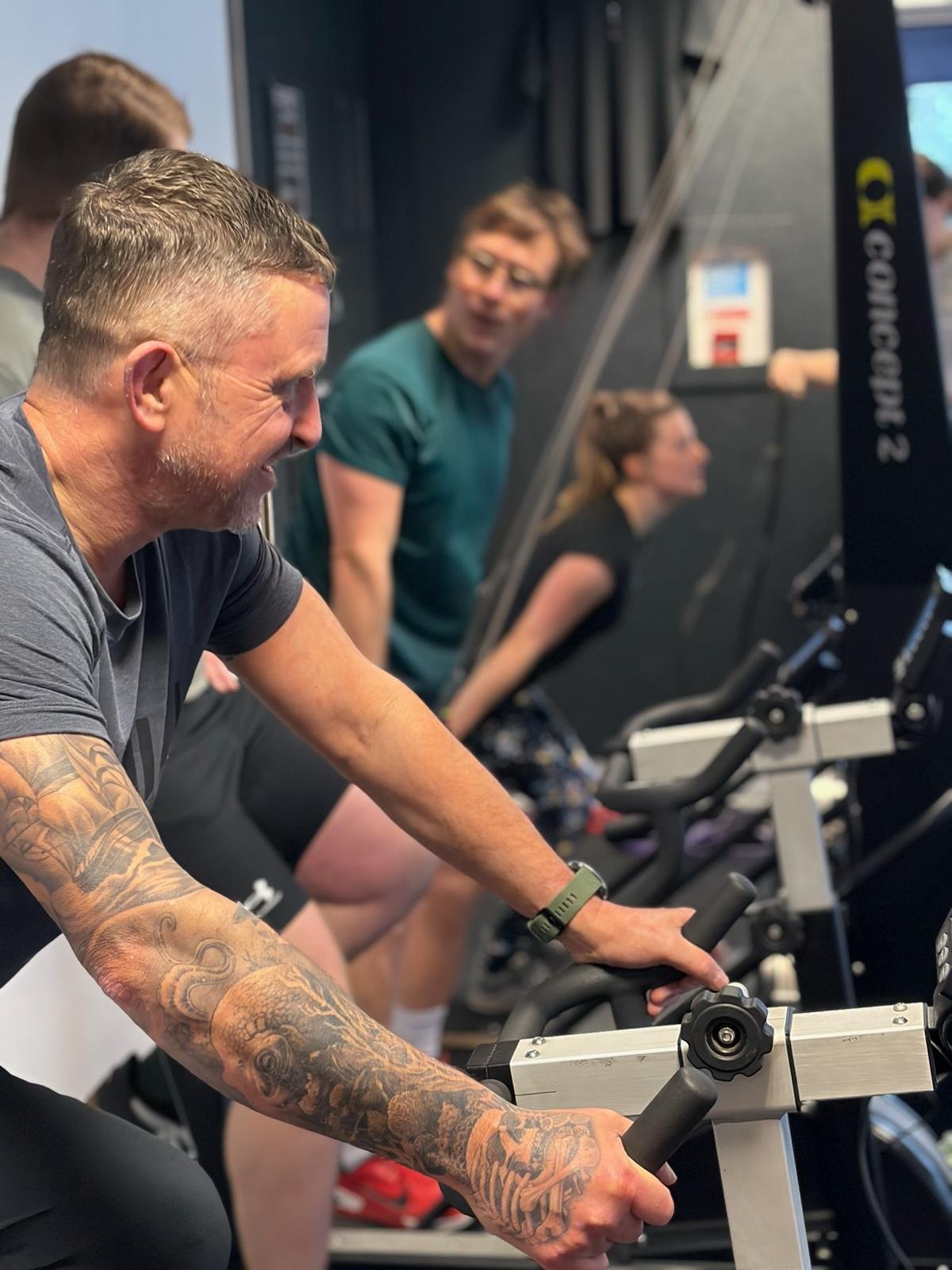 Four people participating in a spin class on stationary bikes at a gym, smiling and engaging with the workout.
