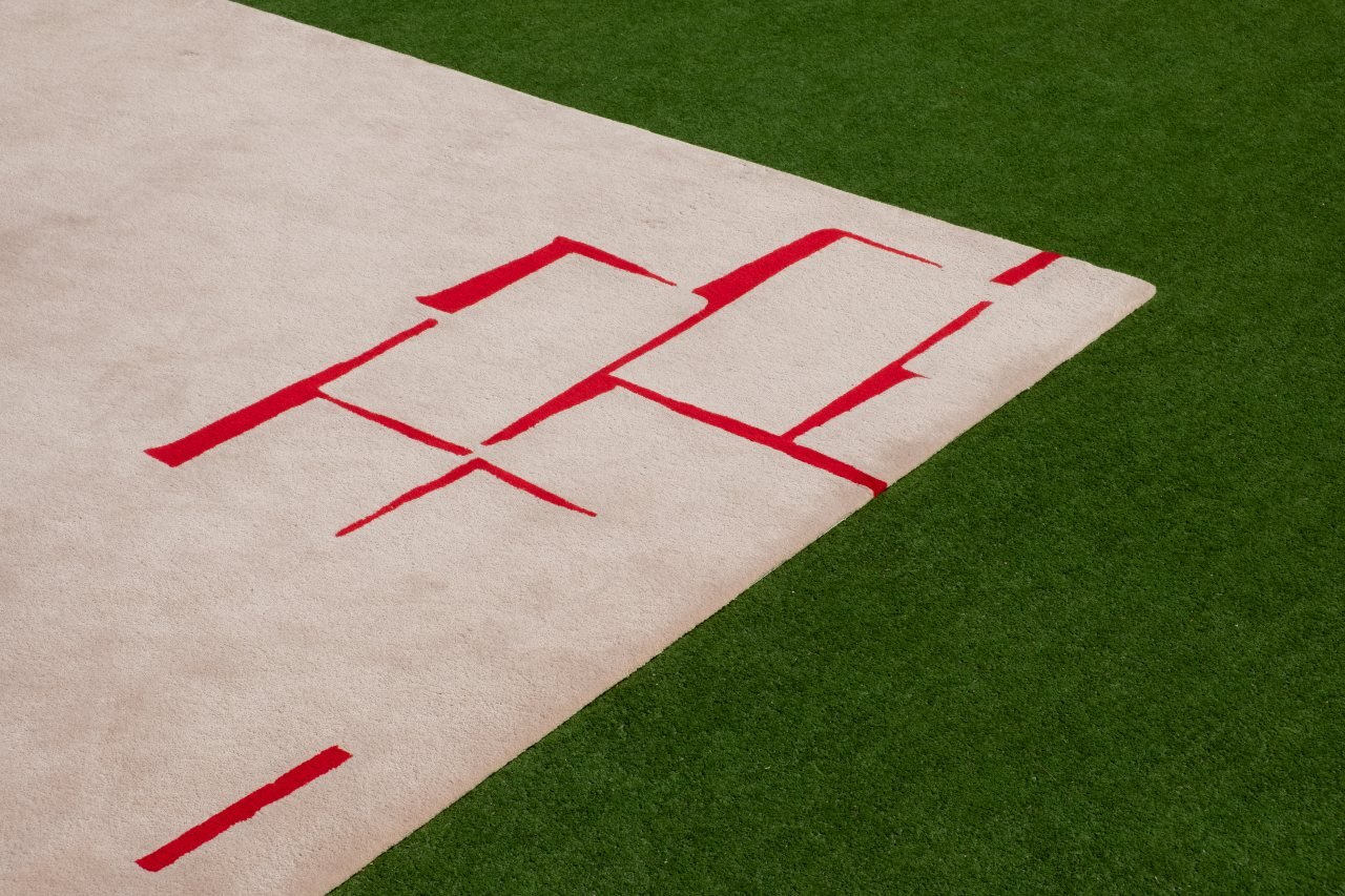 Shifting Pavers Rug in Camel brown and Flame red, made from New Zealand Wool, photographed on green astroturf