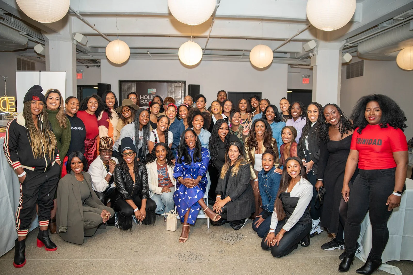 A large group of women gathered indoors for a photo at a holiday event, with some women sitting and others standing, smiling at the camera.