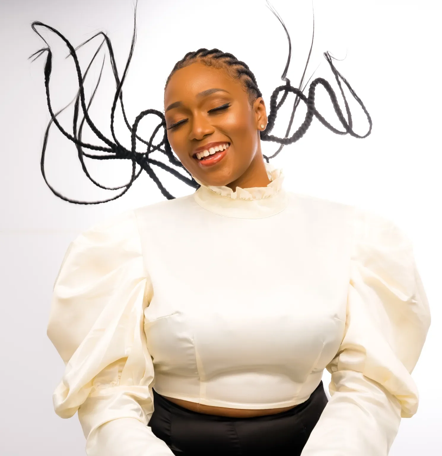 A woman with braided hair and a radiant smile, wearing a white puff-sleeve top, standing in front of an abstract black line art backdrop.
