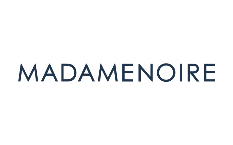 The image shows the logo of MADAMENOIRE, featuring a purple dot above the second 'A' in the word 'MADAMENOIRE' with black text on a white background.