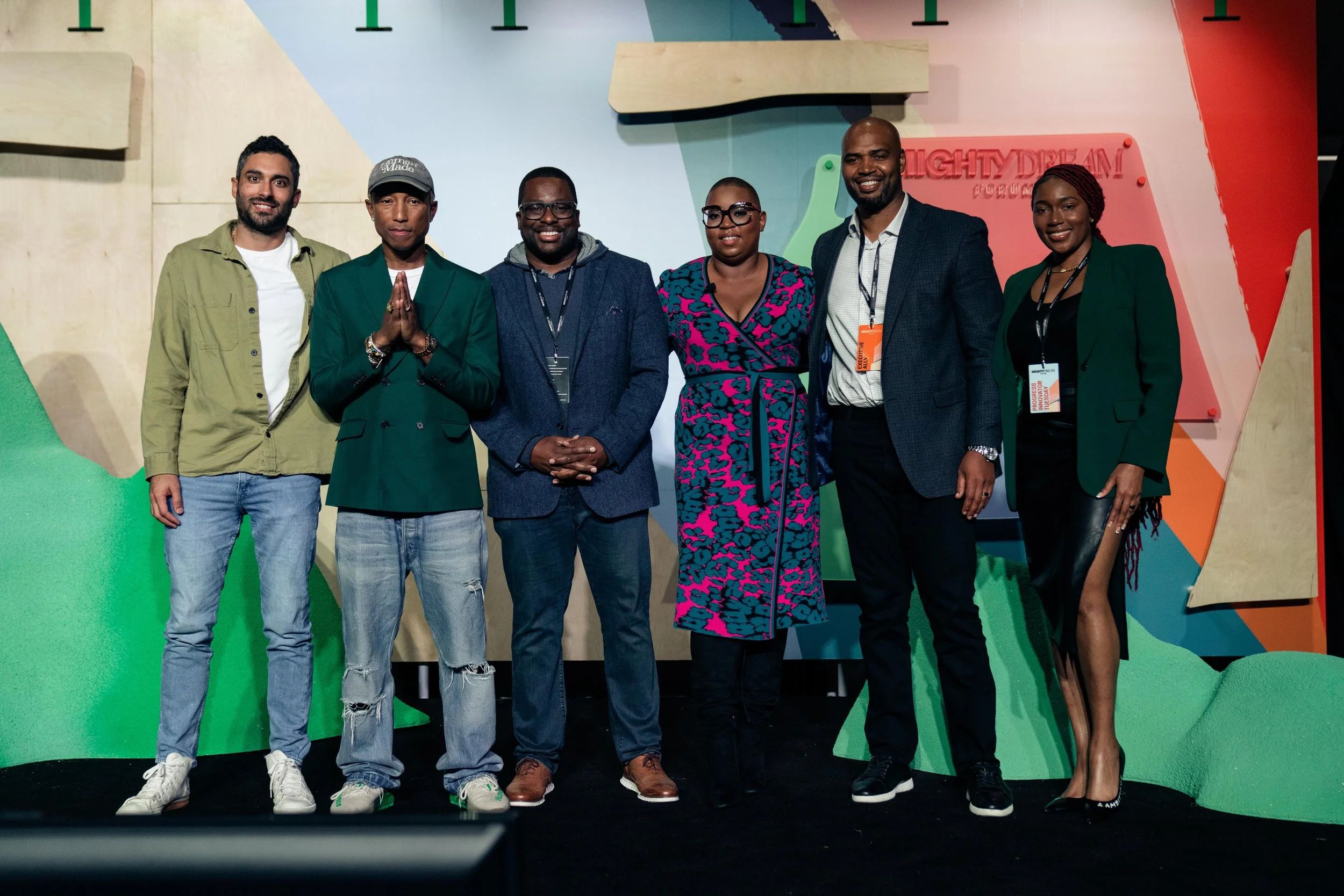 Group of seven diverse people standing together on a stage at a conference or event, smiling for the photo, with colorful abstract background and a sign that says 'FIGHTDREAM'.