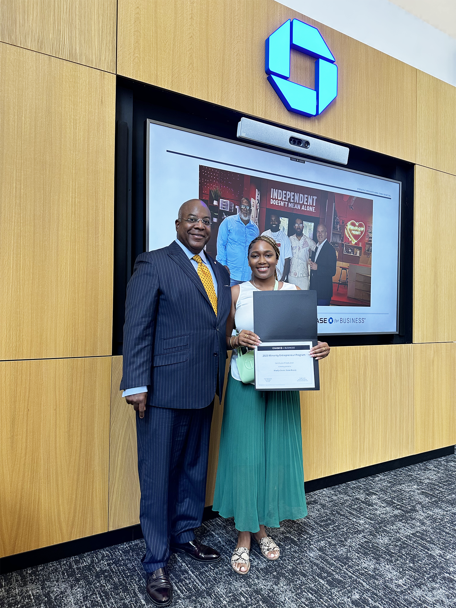 A woman receiving a certificate from a man at a formal event, standing in front of a large display screen with the Chase logo and a group photo on it.