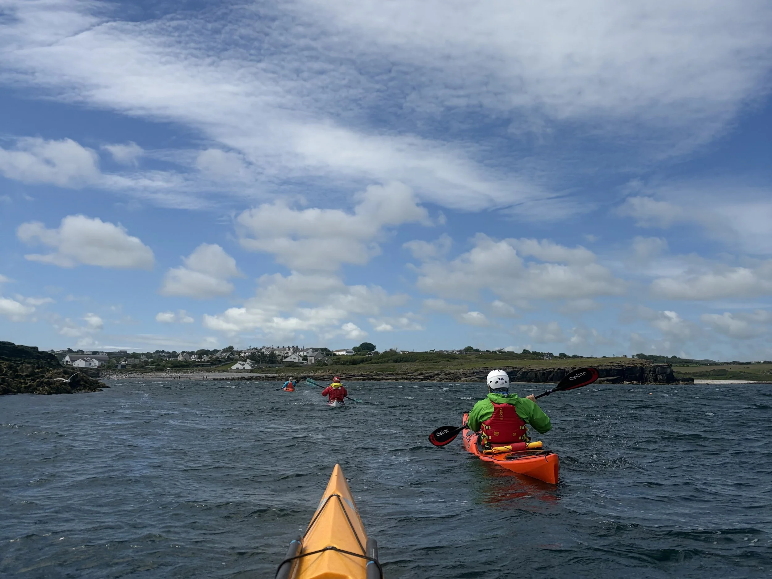 Guide leading a sea kayaking trip beneath cliffs on the Anglesey coastline