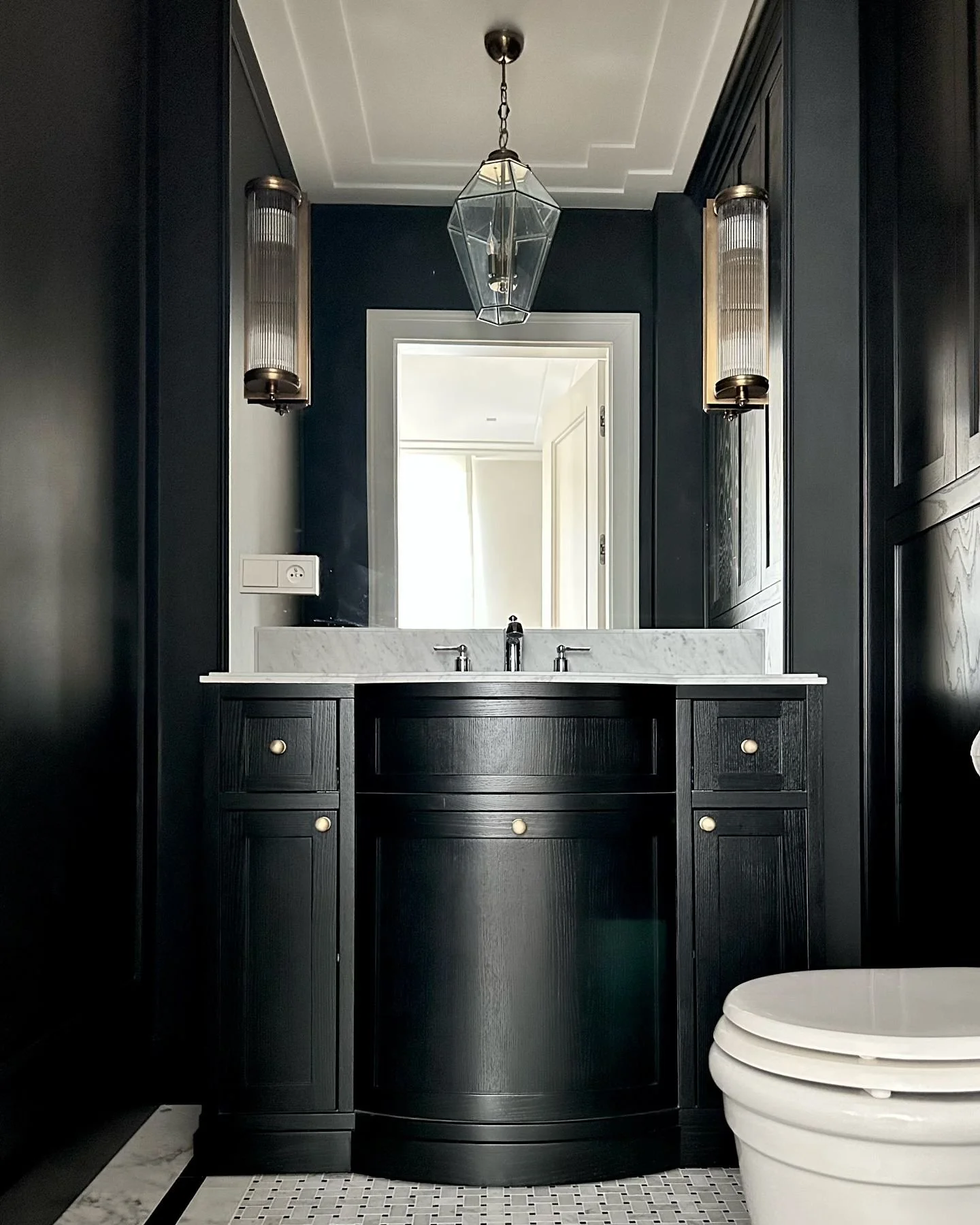 This powder room has not been showcased by us yet. We achieved an incredibly elegant look by using dark wooden panels on the walls. This color scheme creates a sense of intimacy in the room. The elegance is further enhanced by the gold wall sconces a