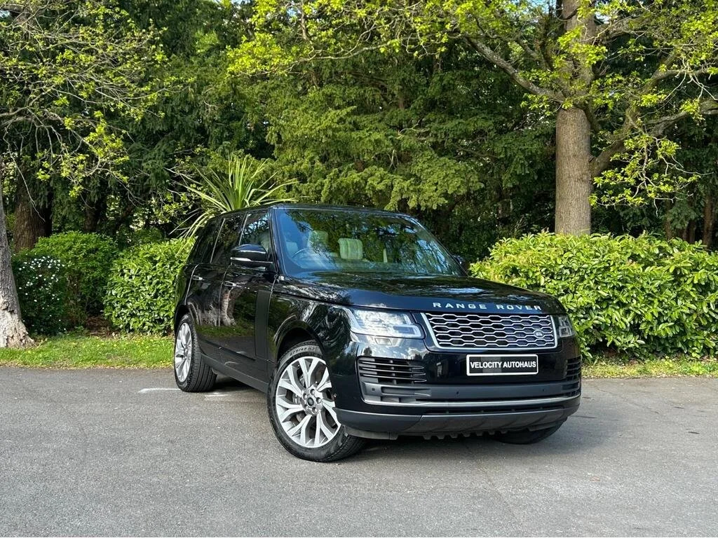 Black Range Rover SUV parked on a paved surface near green bushes and trees.