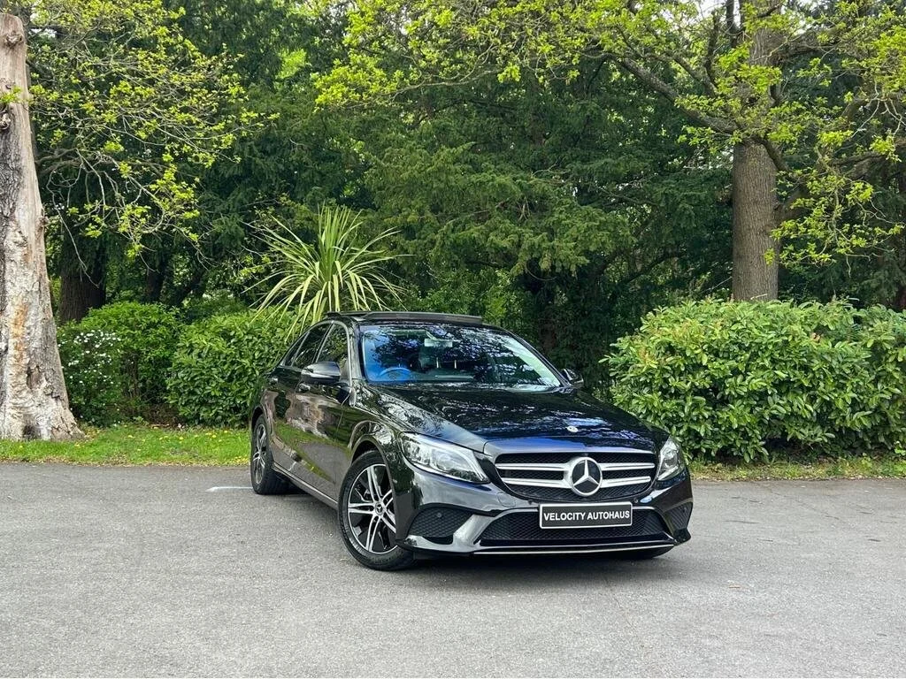 A black Mercedes-Benz sedan parked on a paved surface with green trees and bushes in the background.