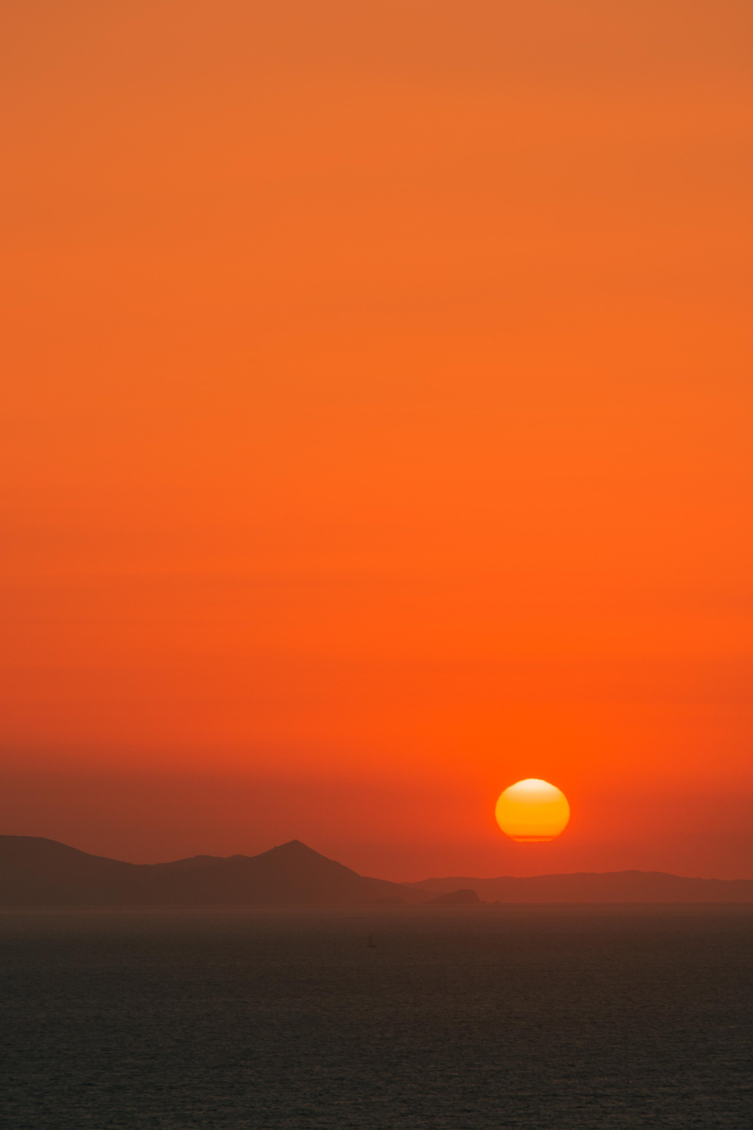 Sunset over a calm sea with an orange sky and distant mountains.