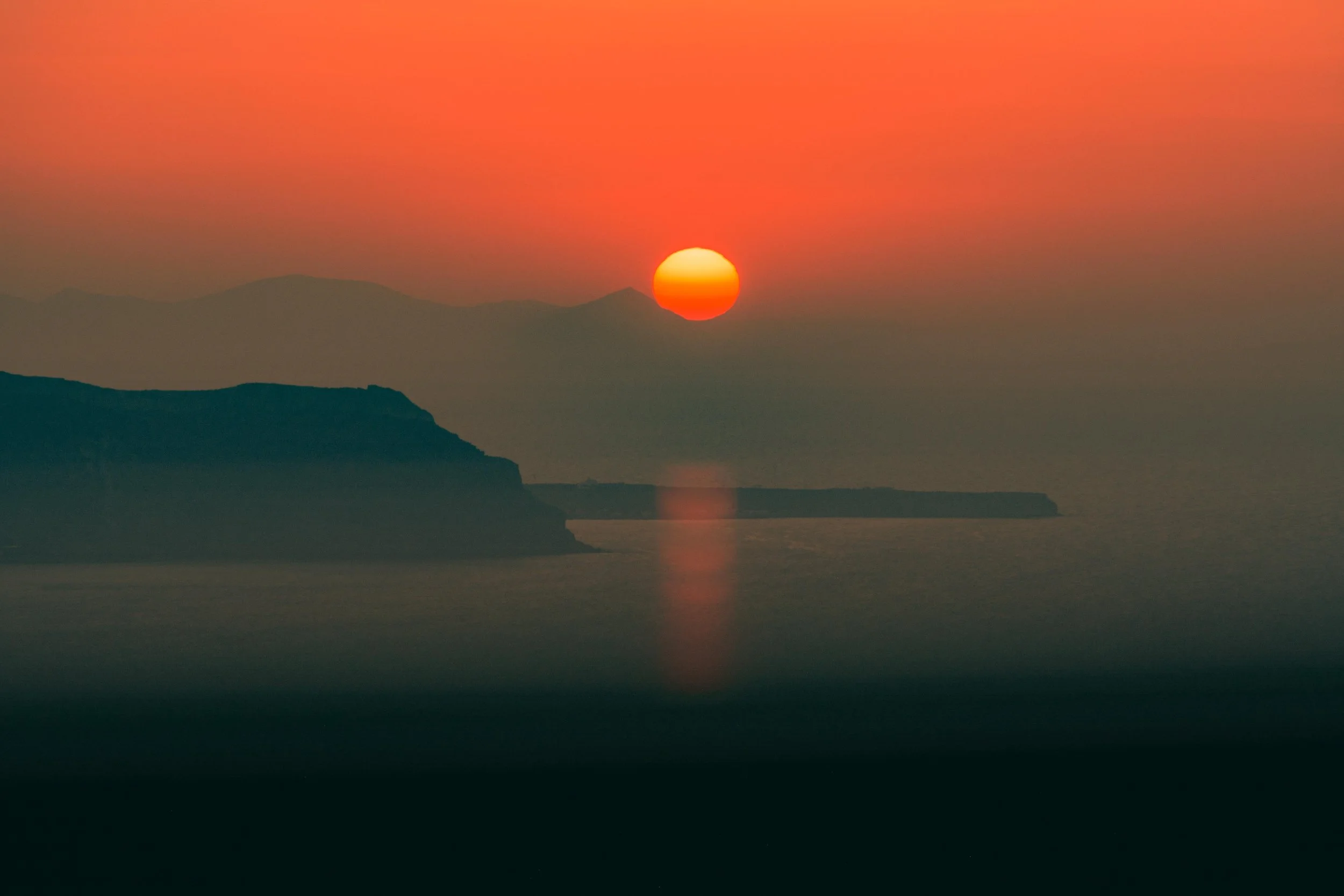 Sunset over calm sea with the silhouette of land in Oia, Santorini 