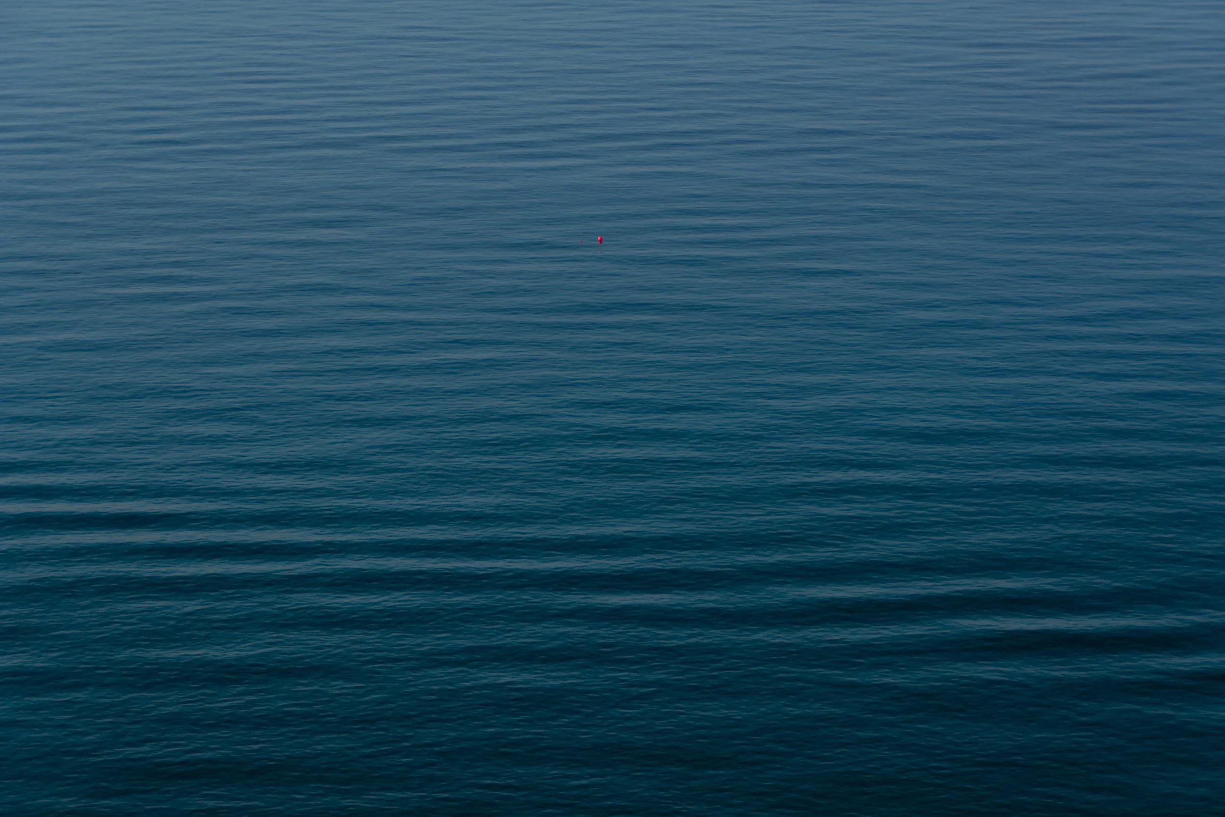 calm sea, deep blue with an orange-reddish buoy floating. 