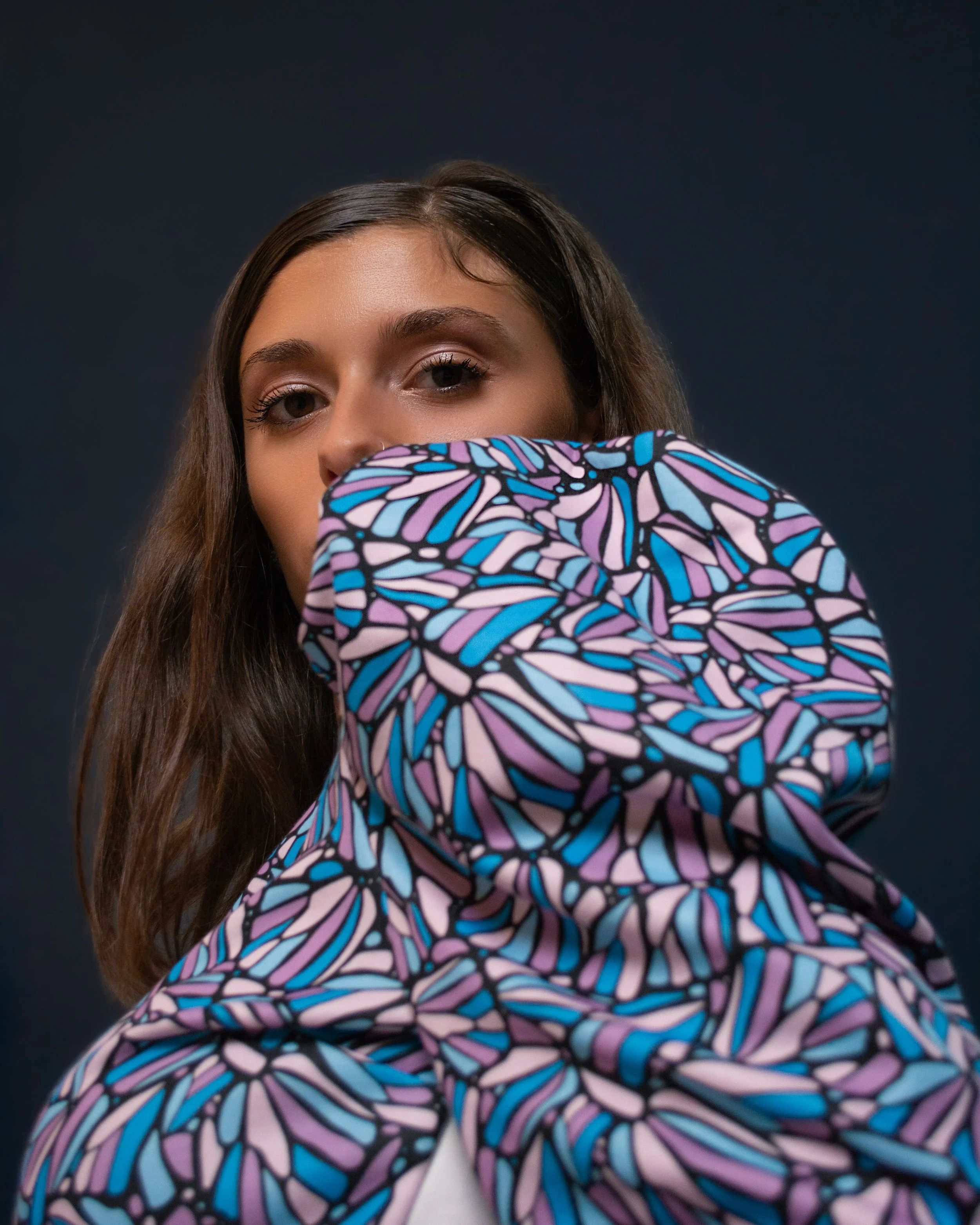 A woman posing looking over her shoulder, wearing a dress with patterned fabric, blue, purple, and pink tones.