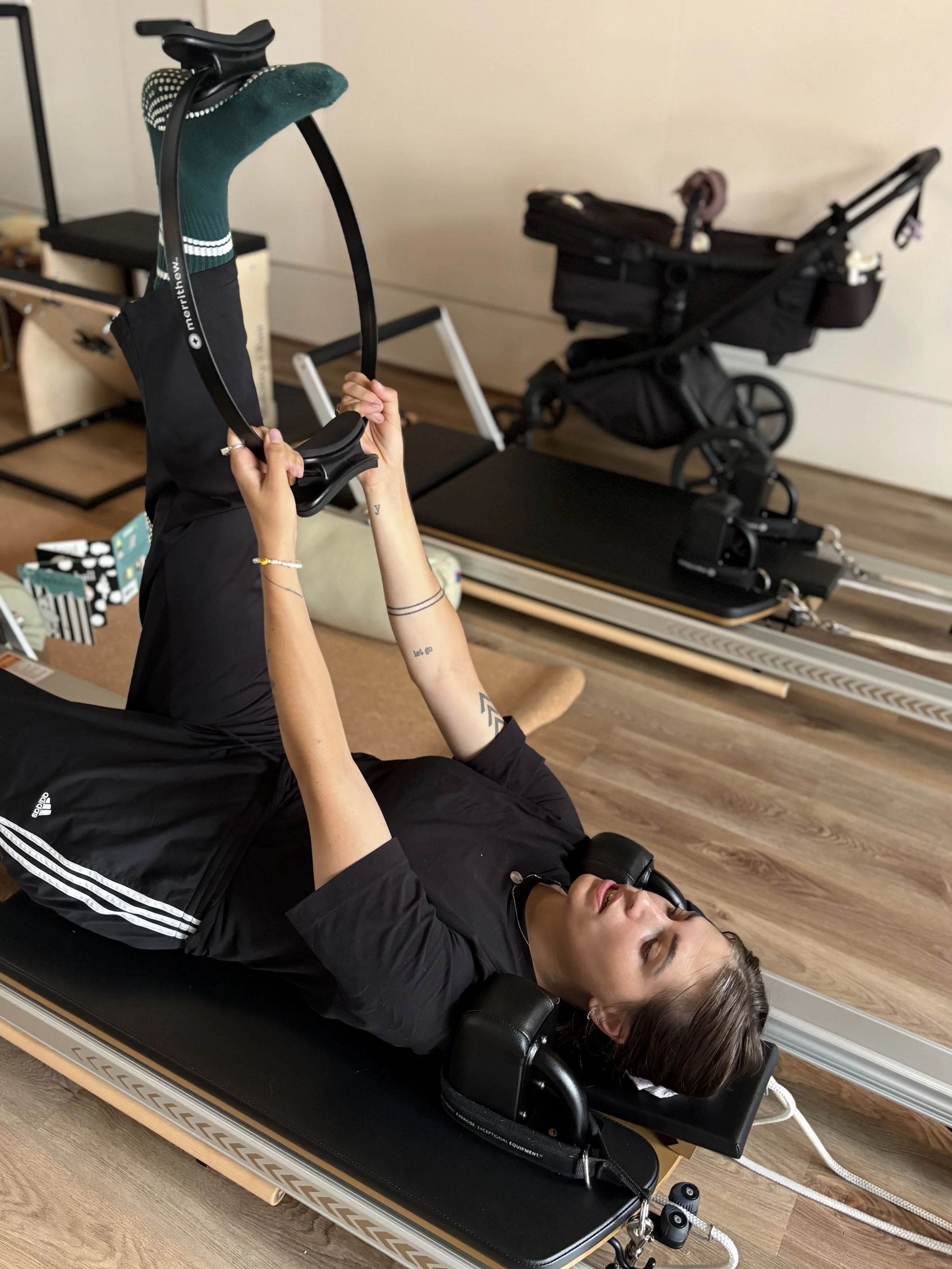 A woman smiling while holding a baby dressed in a polka dot outfit with a fleece vest. They are indoors with fitness equipment in the background.