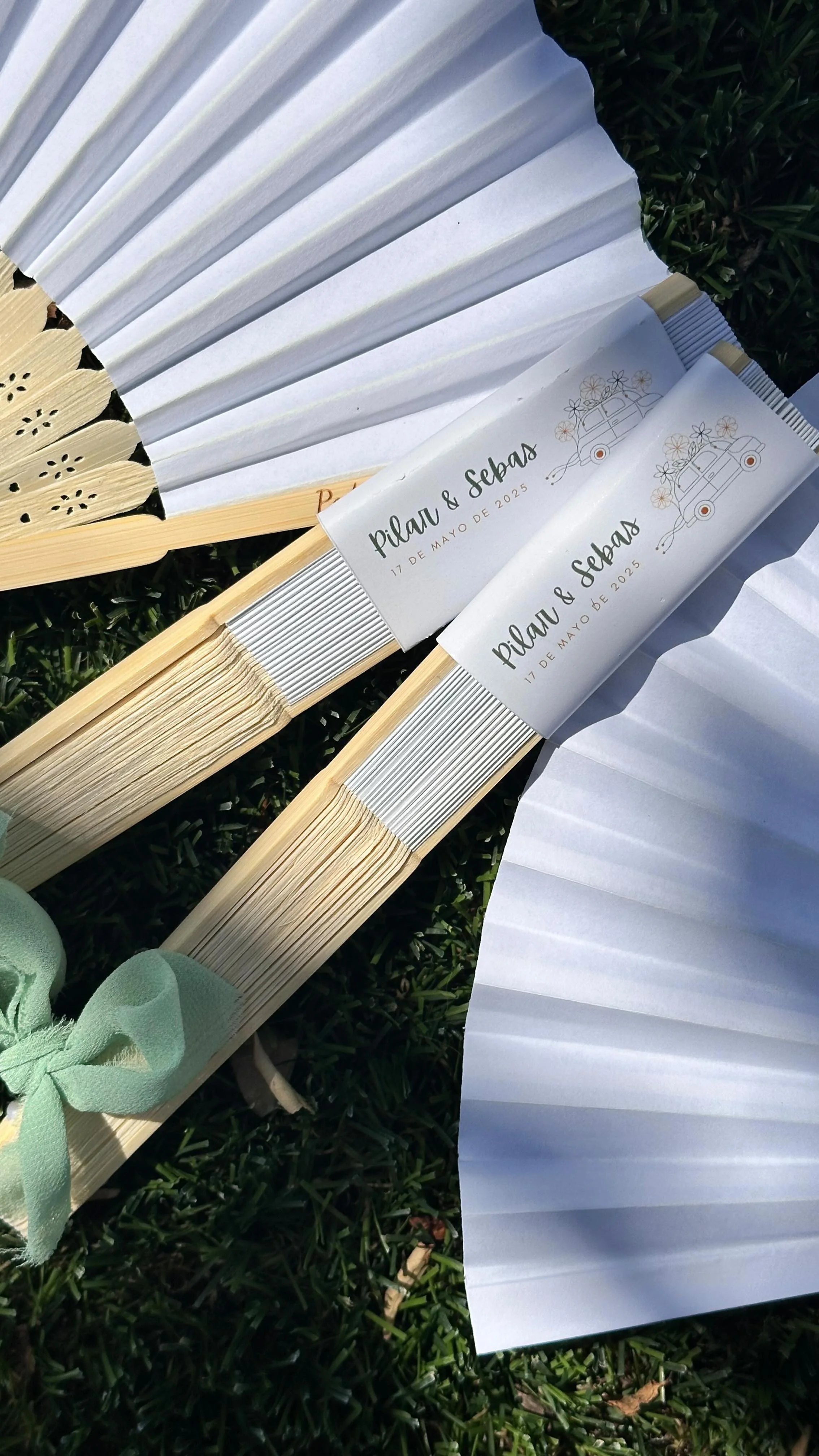 Abanico y serpentinas con invitaciones de boda que dicen 'Pilar & Sebas, 17 de mayo de 2025'.