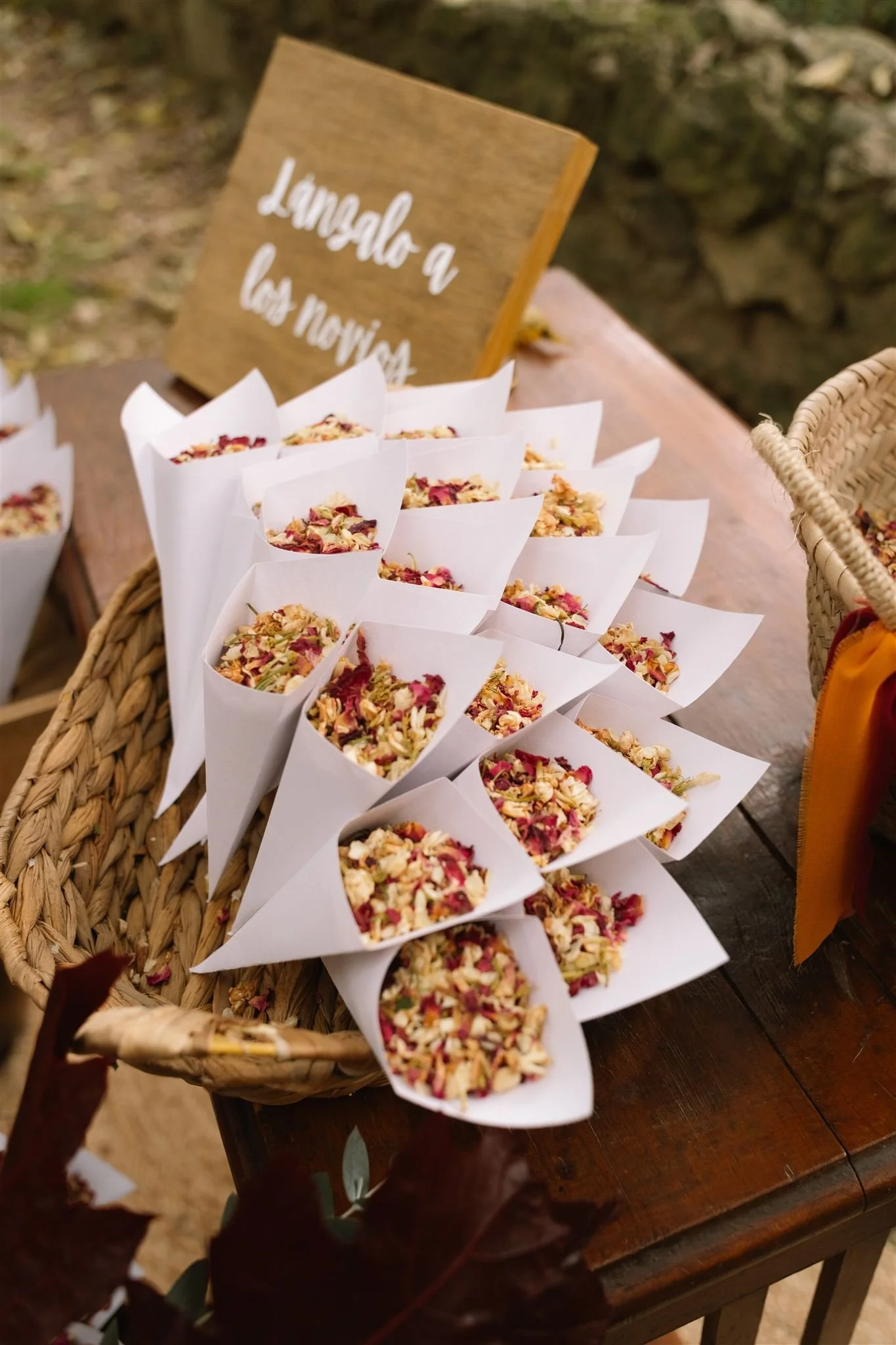 Tazas de papel con pétalos de rosa en un látigo de madera, junto a un letrero de madera que dice 'Lengual a las palabras', en un ambiente al aire libre.
