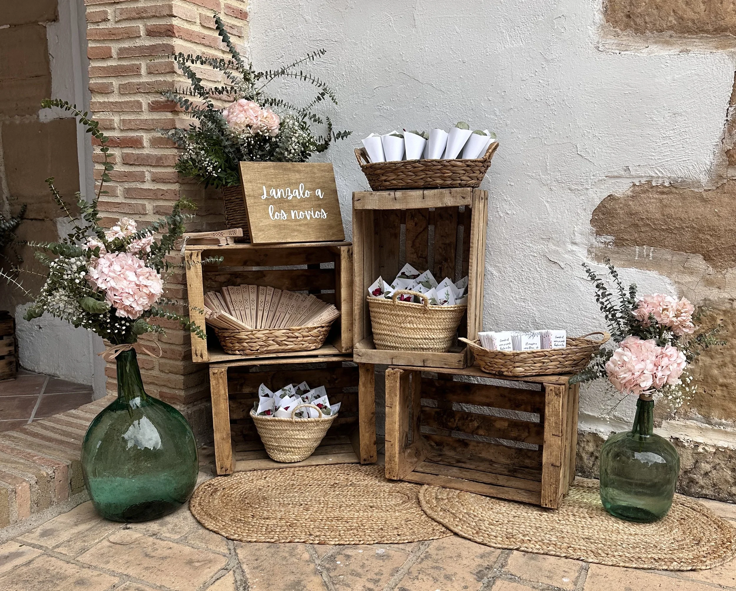 Decoración para boda con flores rosadas y carteles en cestas de mimbre y cajas de madera, con un cartel que dice "lánzalo a los novios".