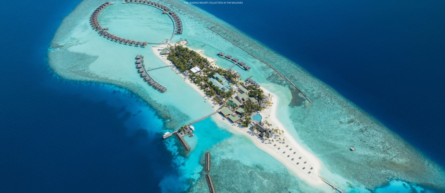 Flygbild av tropisk ö med resort, strand och bungalower i havet.