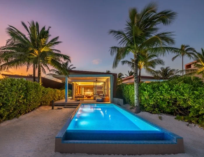 Lyxvilla med privat pool, belyst på kvällen, omgiven av palmträd och grönska.