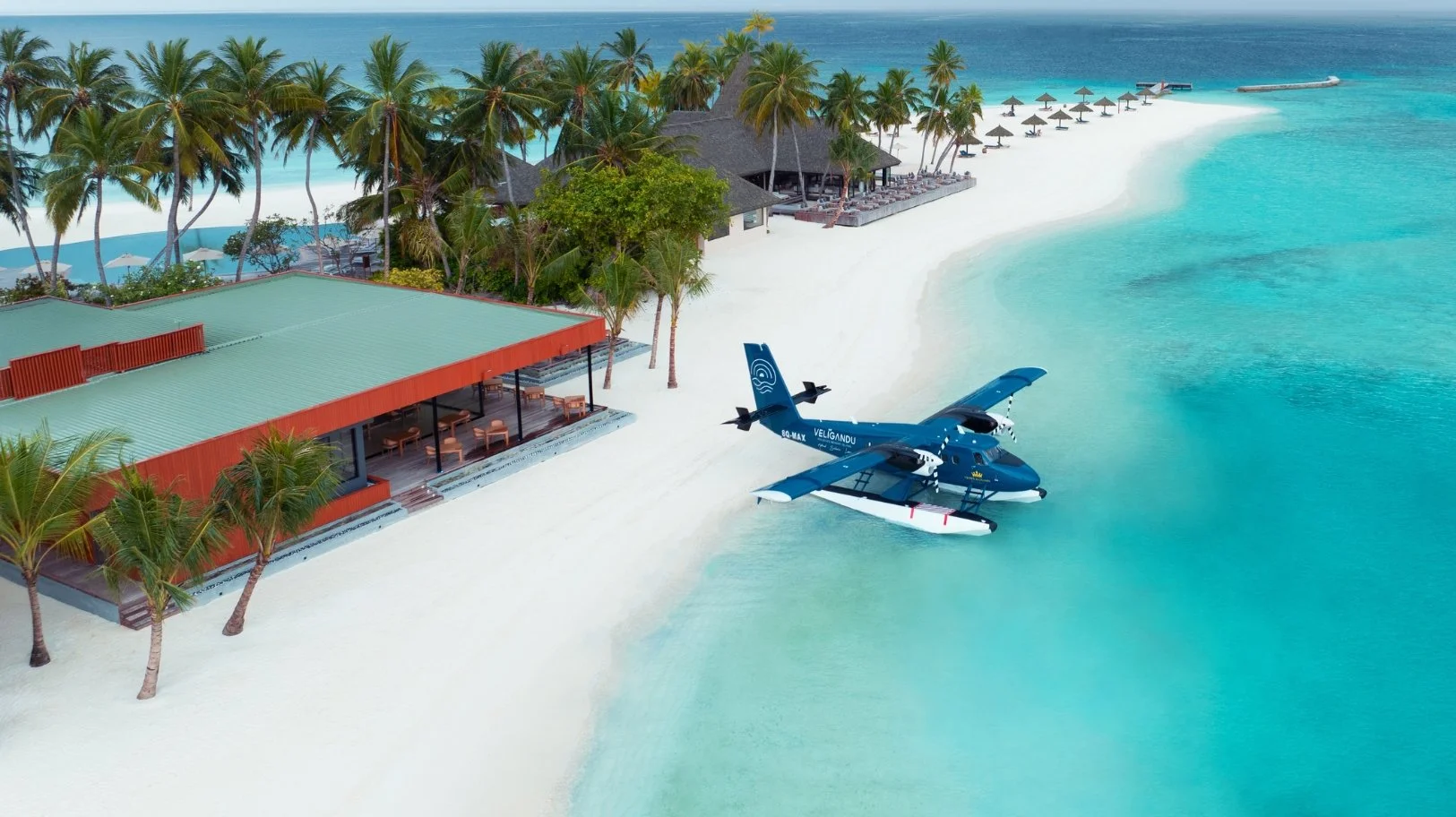 Sjöflygplan vid tropisk strand med palmer och resort.