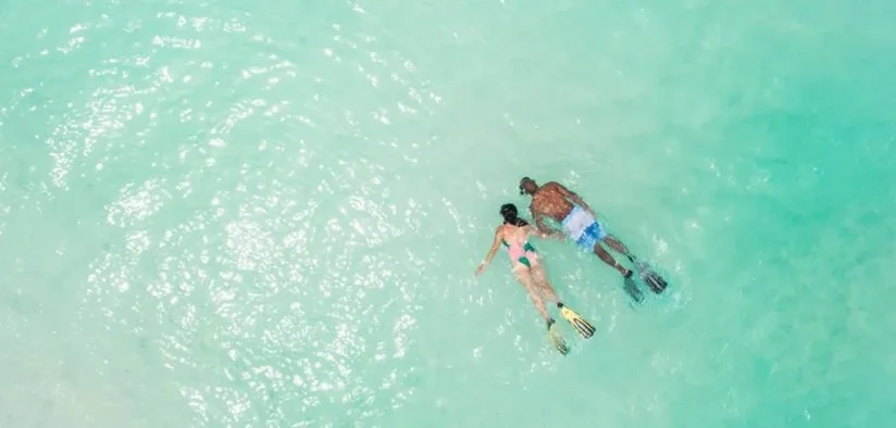 Två personer snorklar i klart turkost vatten.