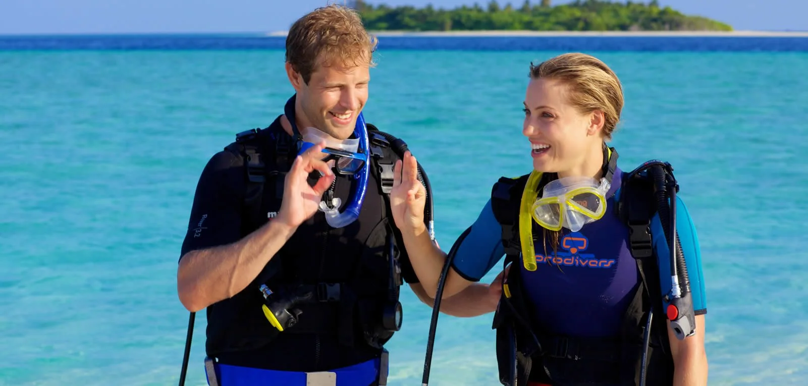 Två personer iförda dykutrustning på Maldiverna står vid havet och ler mot varandra.