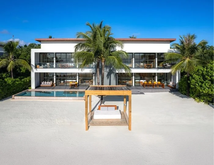 Modern villa vid stranden med palmer, pool och solstolar.