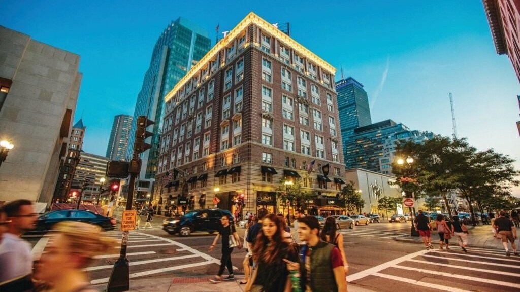 Stadsgata i skymningen i Boston med höghus och gående människor.