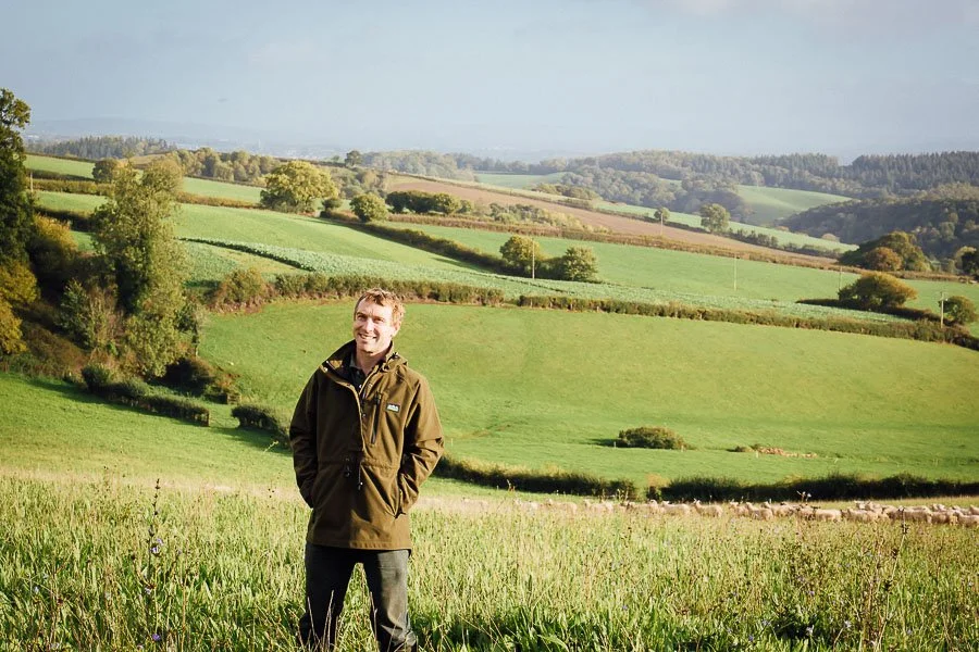 Chris stood in grass field with rolling countryside behind