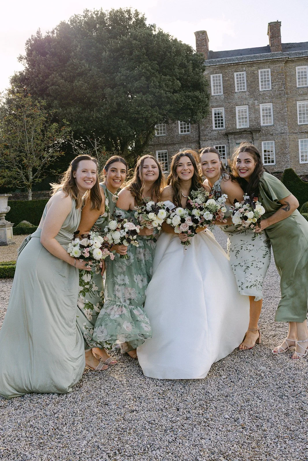 bride and bridesmaids in sage green dresses holding blush ivory and burgundy stylish bouquets