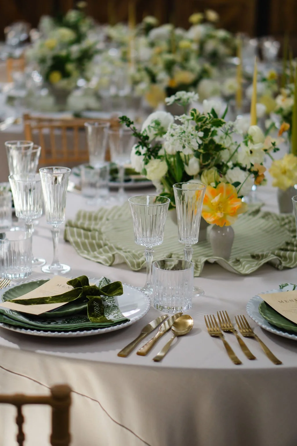 long tablescape full of butter yellow spring flowers in ceramic urns, with green velvet ribbon, cut glass and stripe green linen