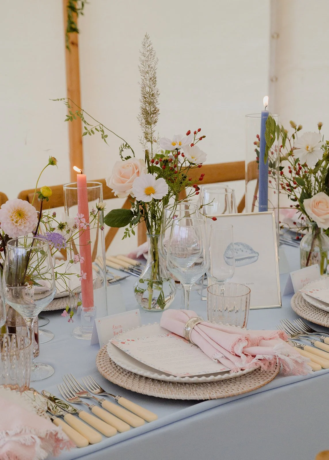 long banquet wedding tables full of seasonal flower bud vases, coloured taper candles and coloured linen