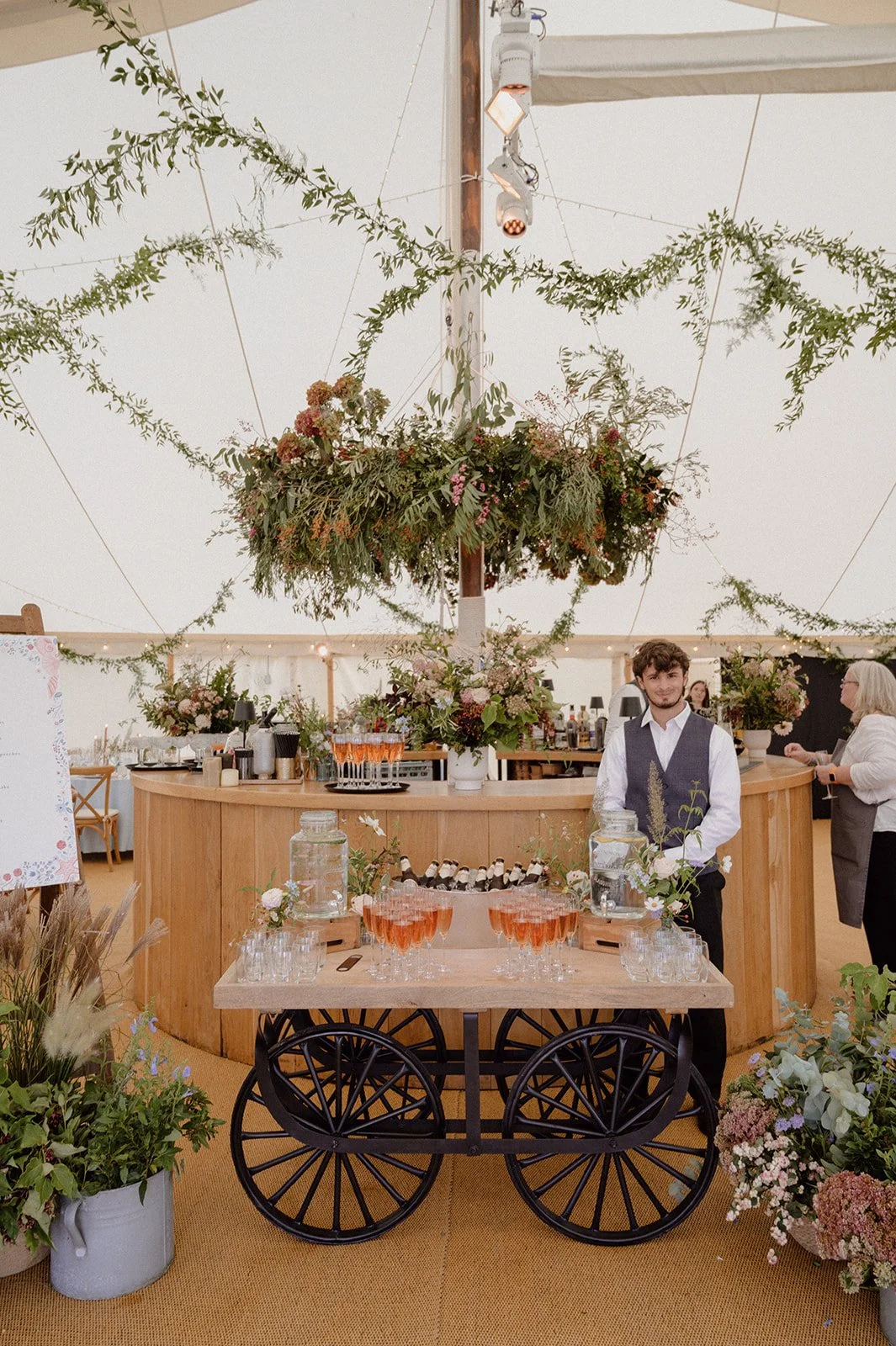 marquee bar flower installation with baskets of seasonal flowers and hanging chandelier