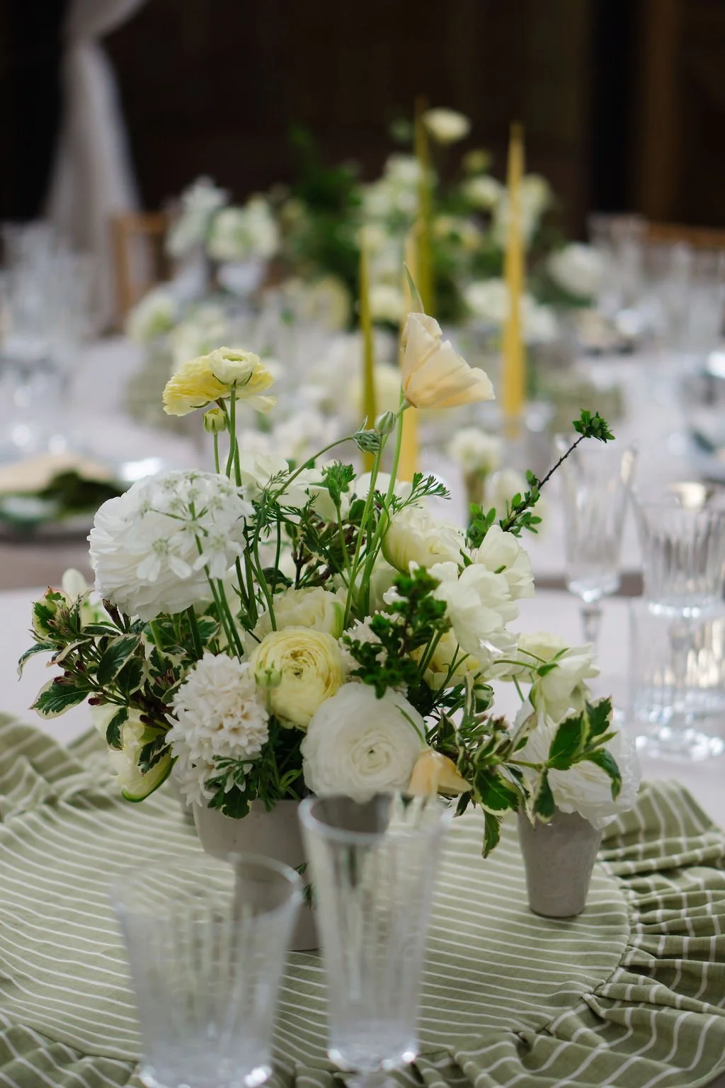 butter yellow spring flowers in low ceramic urn on a wedding tablescape with striped linen
