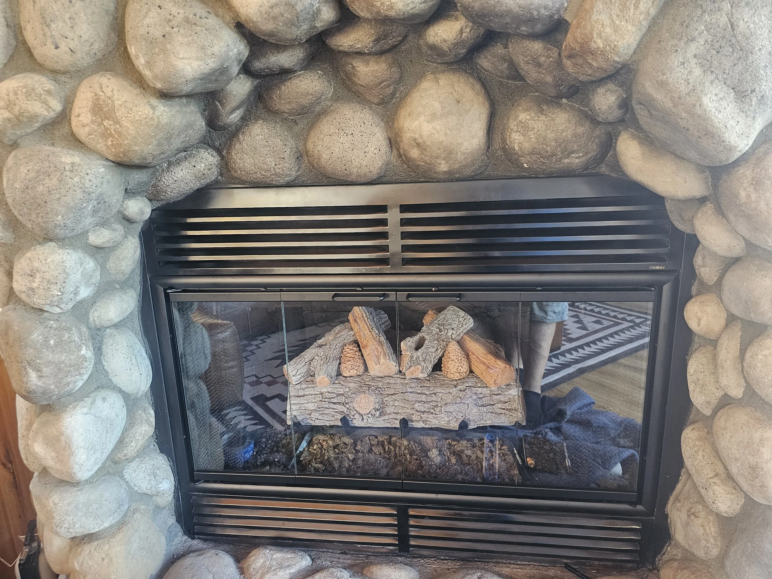 Stone fireplace with wood logs inside, black metal frame, and a glass door.