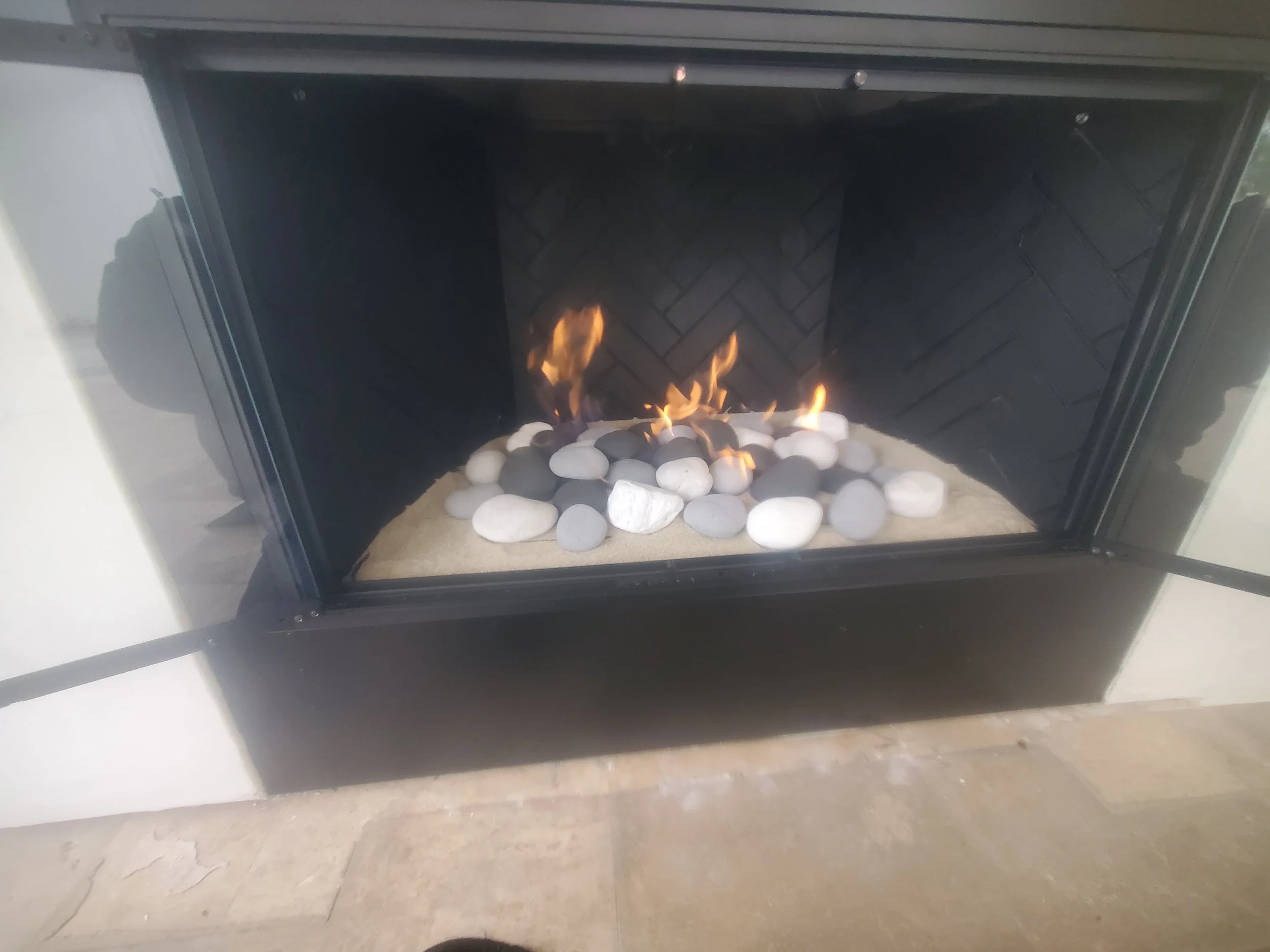 A fireplace with a bed of white and gray stones and small flames burning among them.