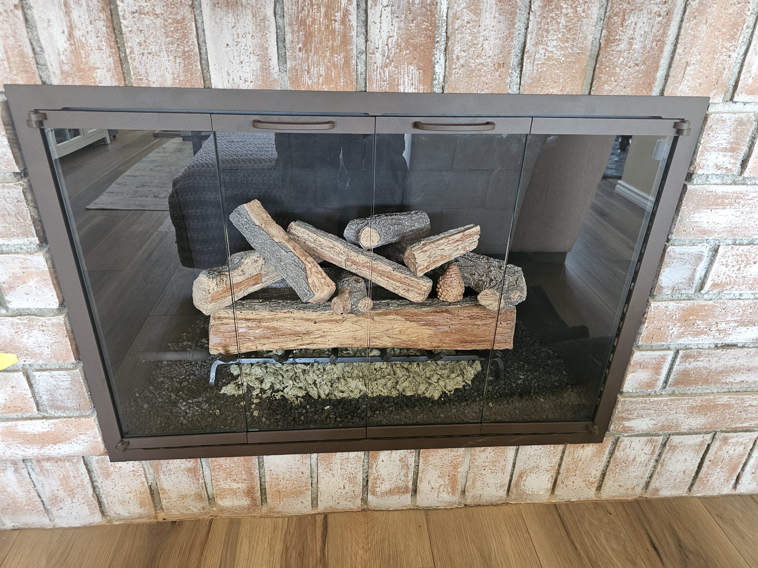 Wood-burning fireplace with stacked logs inside, set into a brick wall.