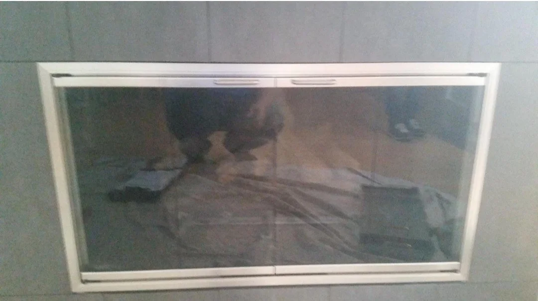 A rectangular vent or grille on a wall with a person's reflection visible on its surface.