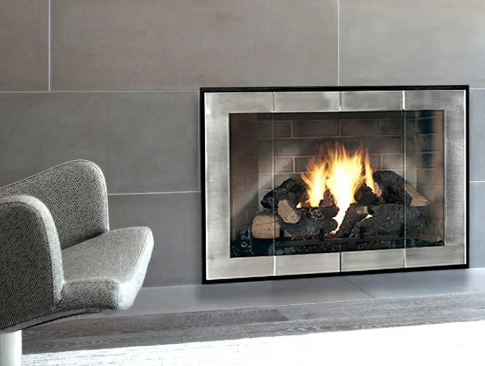 A modern living room fireplace with a fire burning inside, surrounded by gray tiles and a black metal frame, with a light gray upholstered chair nearby.