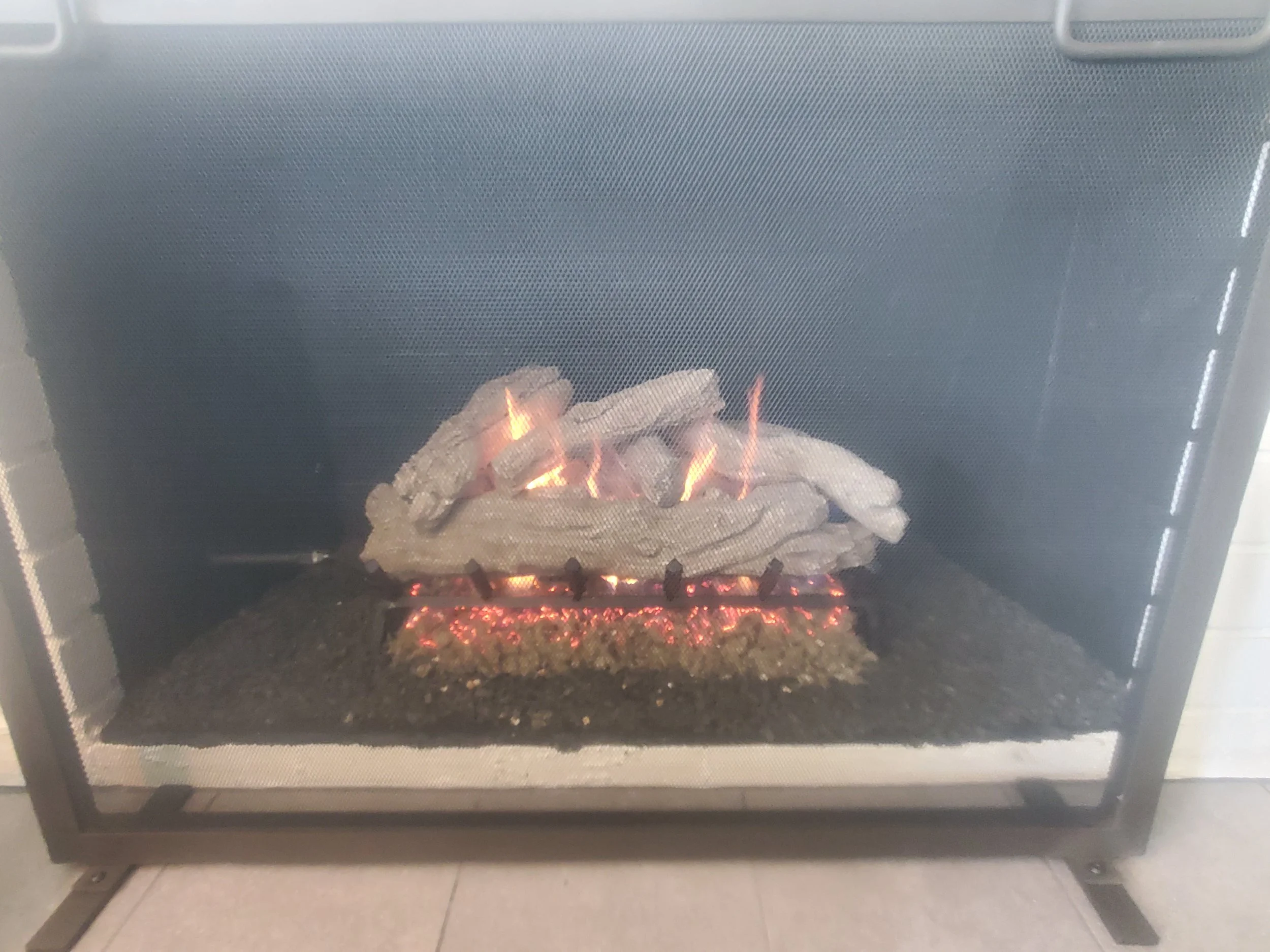 Gas fireplace with artificial logs burning, glowing embers, and flames inside a black metal frame.
