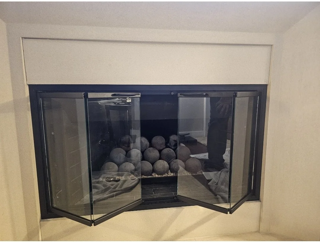 A fireplace with glass doors, filled with decorative black stones.