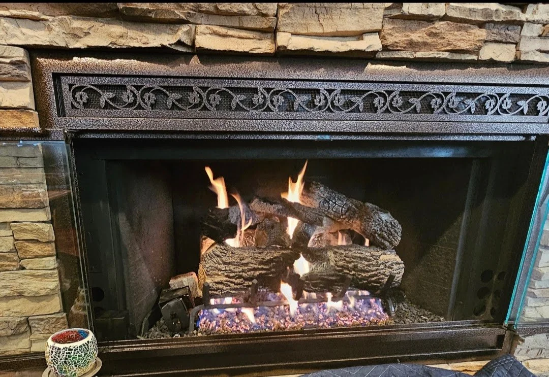 A cozy fireplace with burning logs set in a stone surround, with a decorative iron grate at the top.
