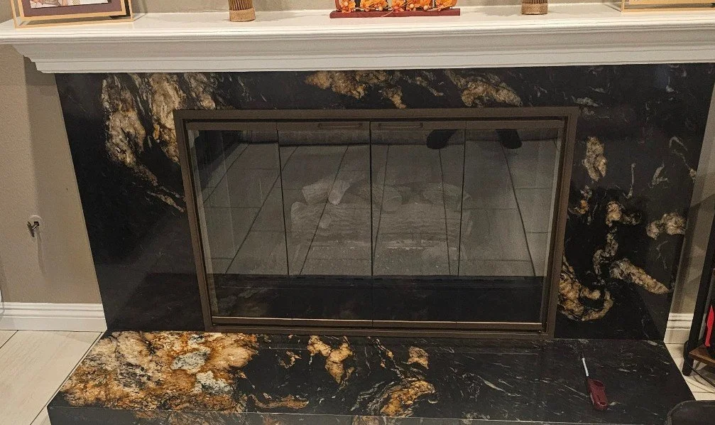 A fireplace with a black and gold marble surround and glass doors.