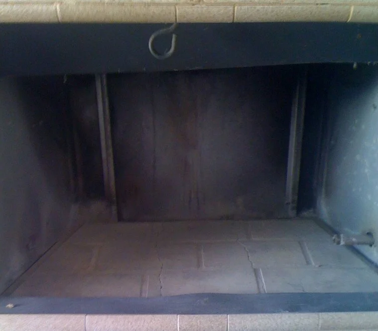 Empty fireplace with a tiled floor and soot-stained blackened brick interior.