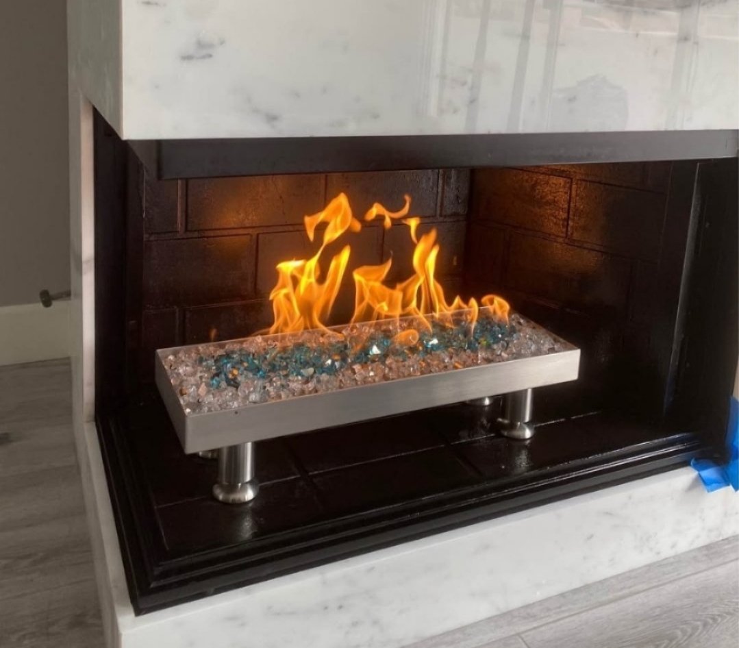 A modern fireplace with a metal fire grate and decorative glass stones, built into a marble surround.