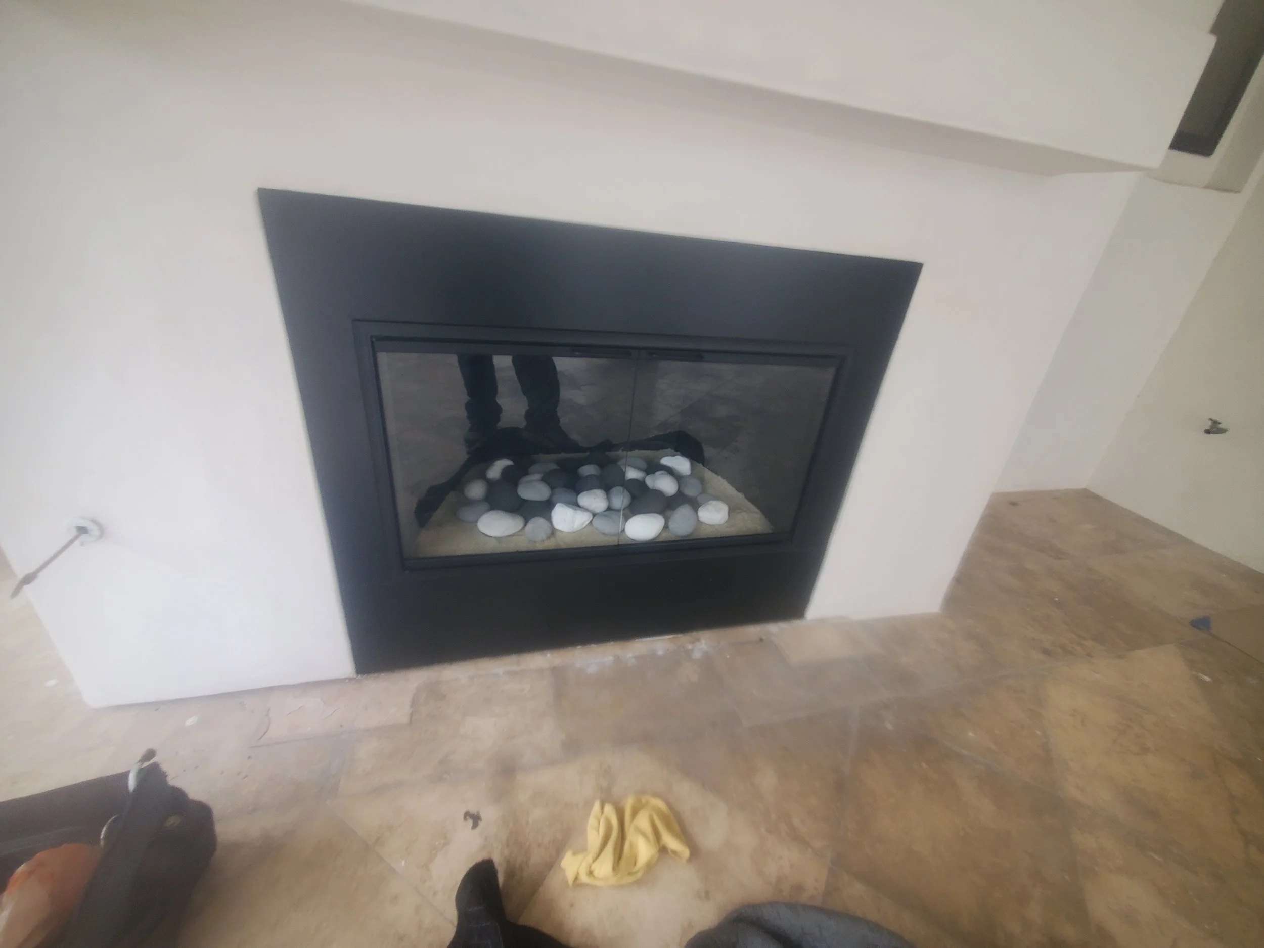 A modern fireplace with black frame and white stones inside, surrounded by white wall and wooden flooring.