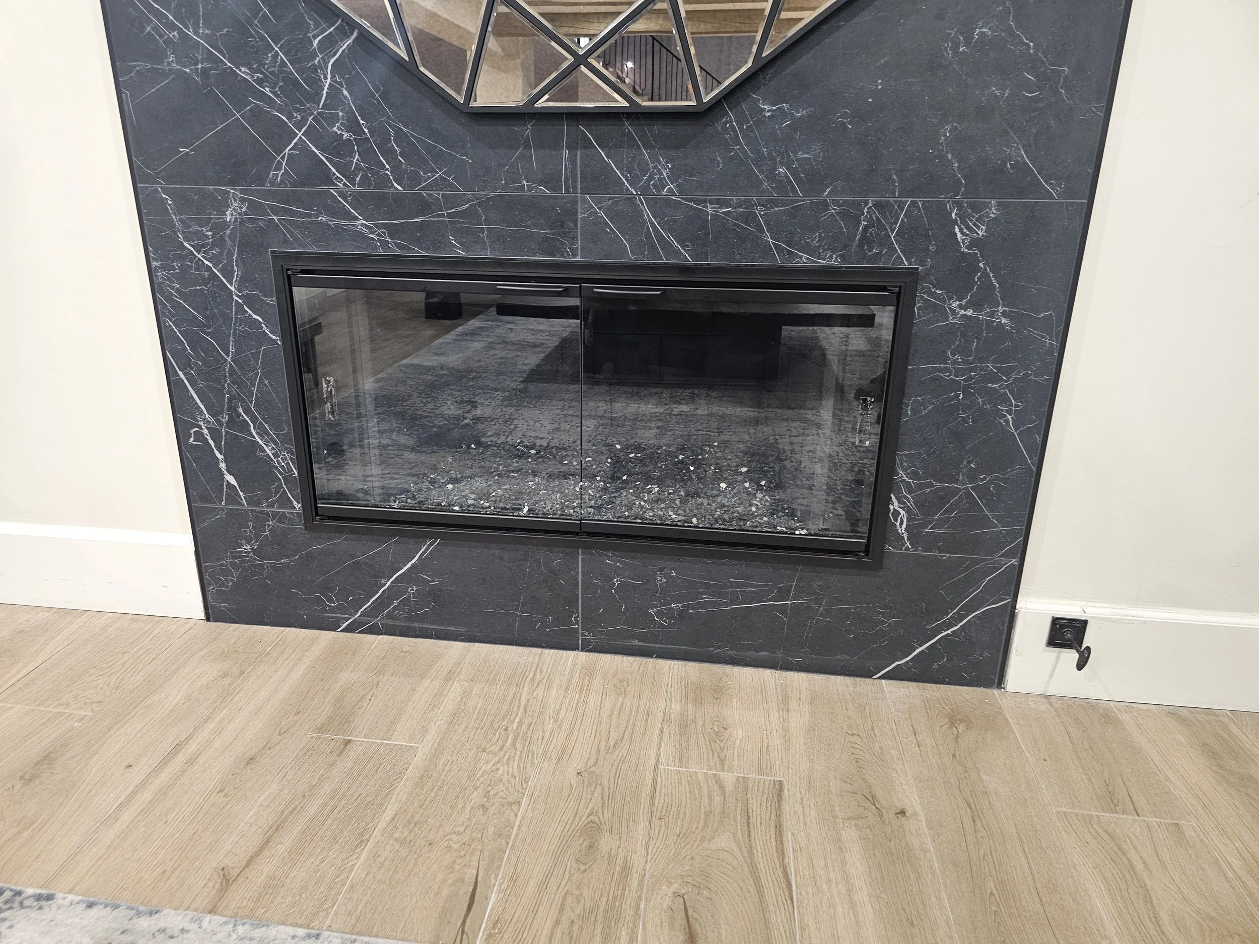 Modern fireplace with a black marble surround and reflective glass doors, situated on a light wood floor.