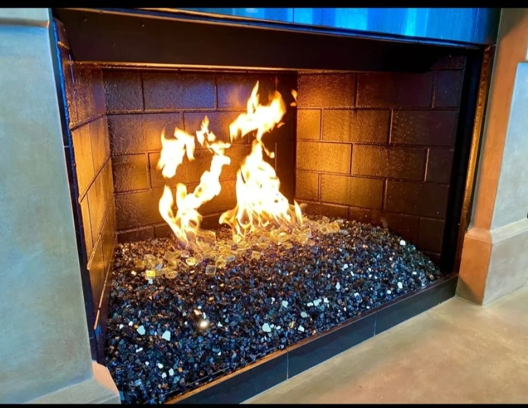 Gas fireplace with flames and decorative black stones inside a brick-lined fireplace.