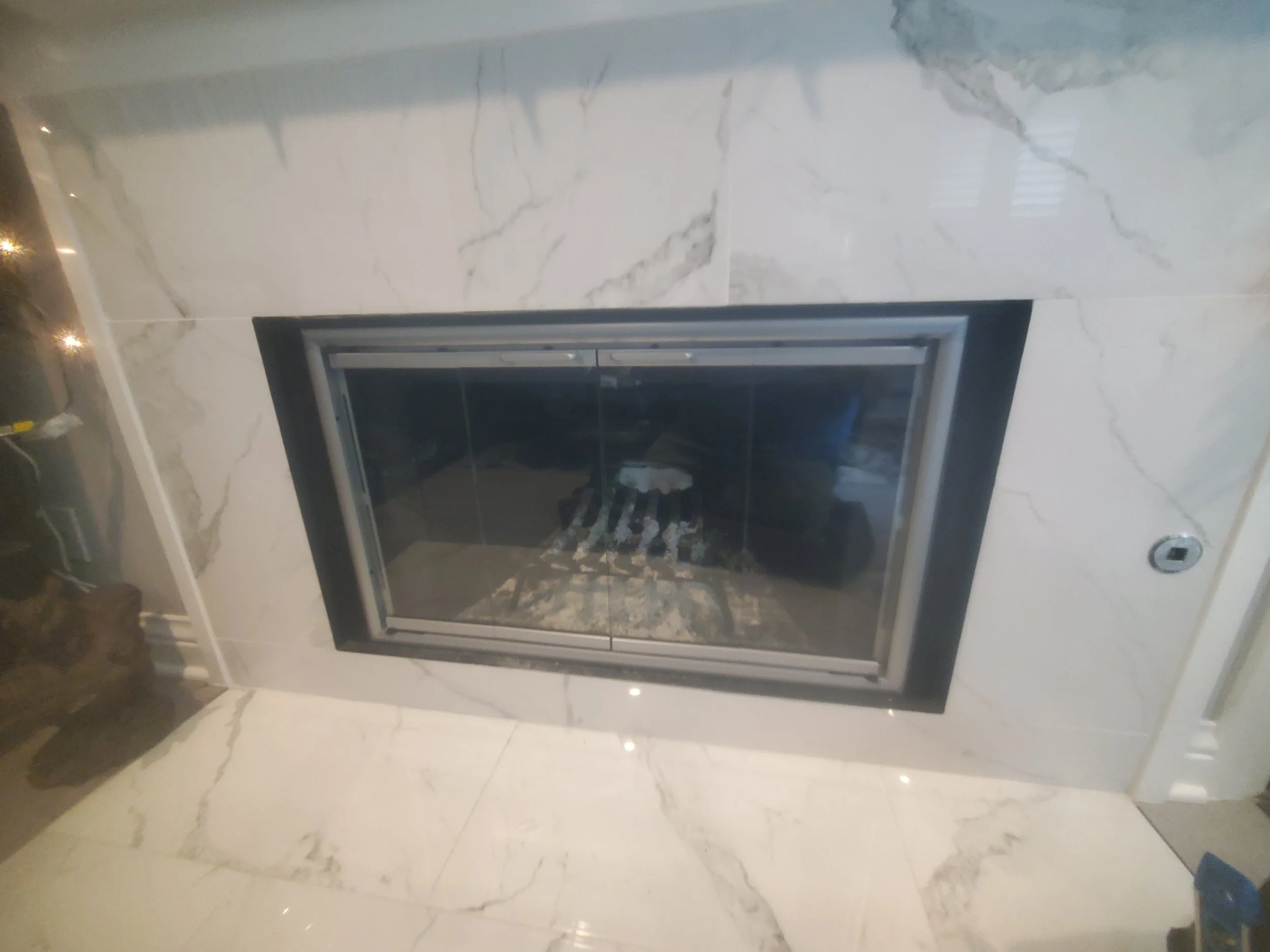 Modern fireplace with black frame set in a wall with large white marble tiles featuring gray veining.