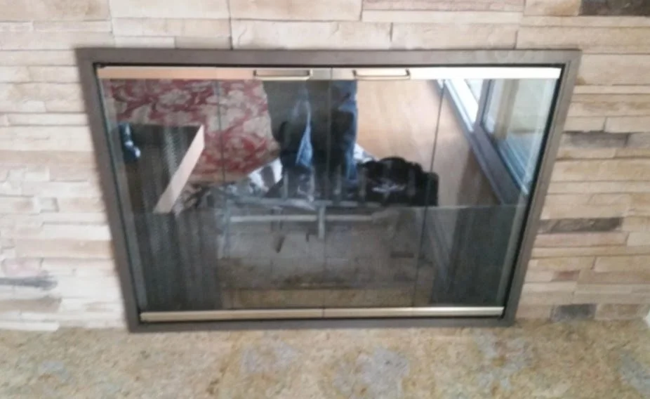 A fireplace with a glass door set into a stone wall, reflecting the room and a person taking the photo.
